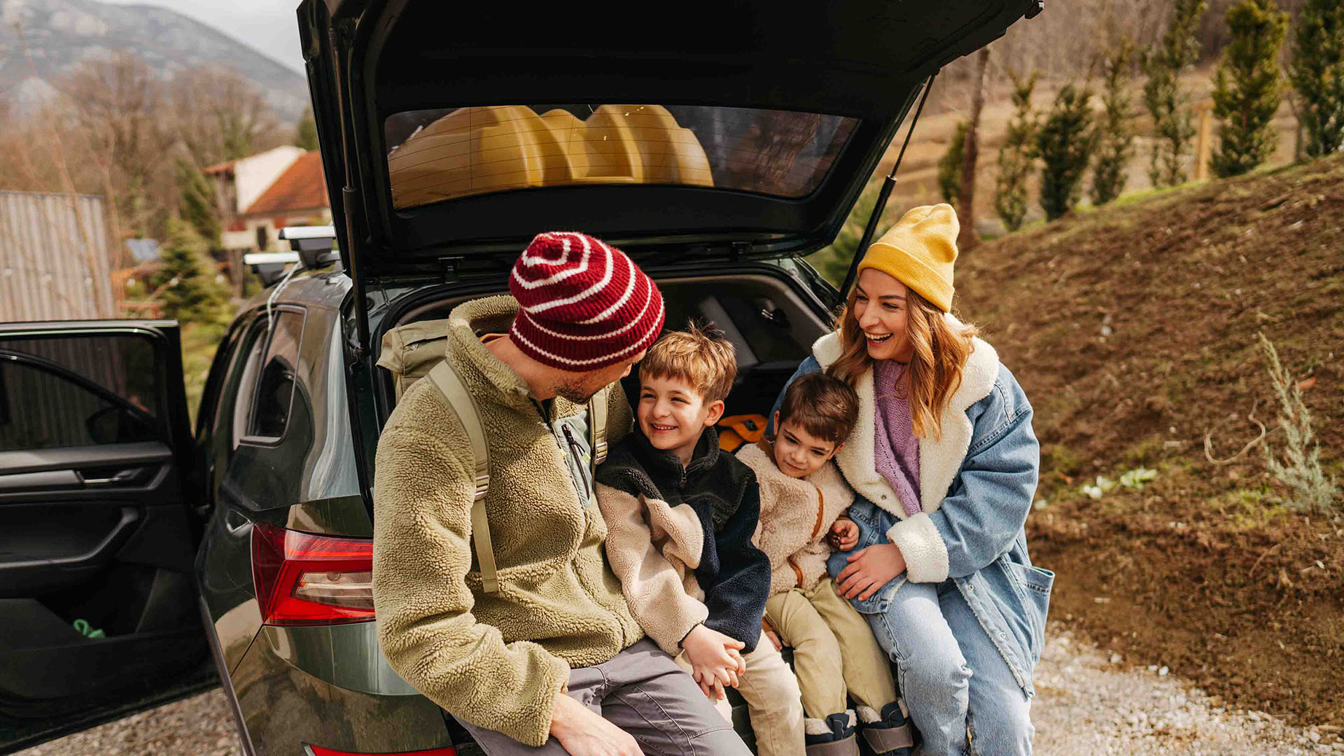 Family taking a break at the open tailgate of an SUV during a road trip.