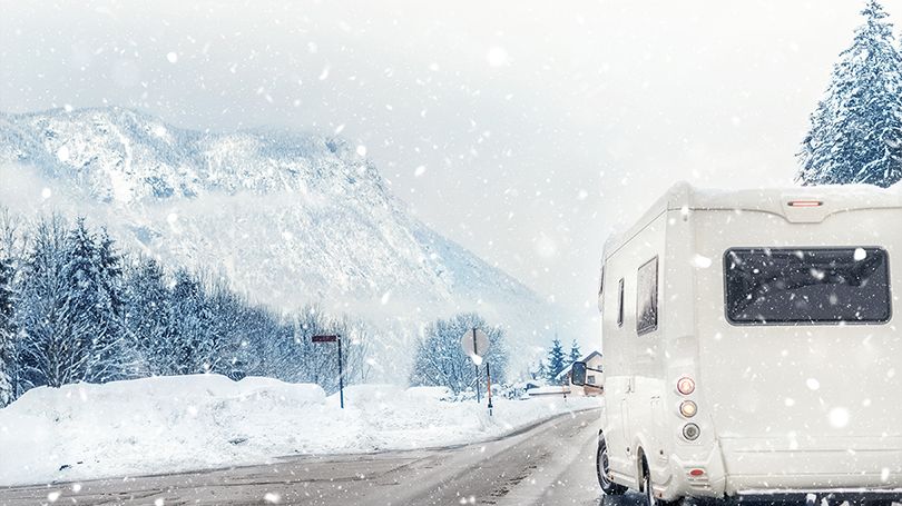 An RV driving on the road through the snowy mountains