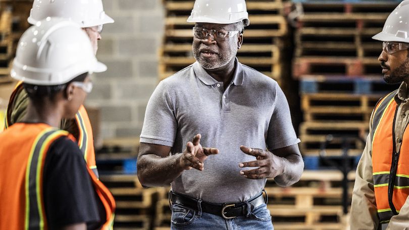 Black male executive speaking with workers.