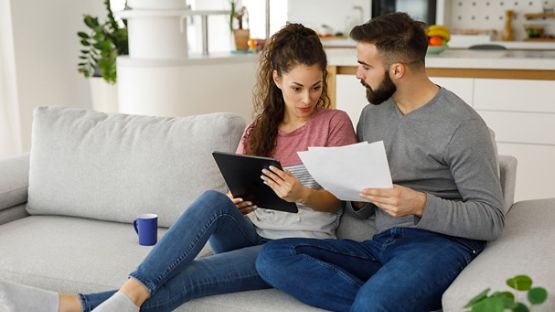 A couple sitting on a sofa in their living room making a checklist. 