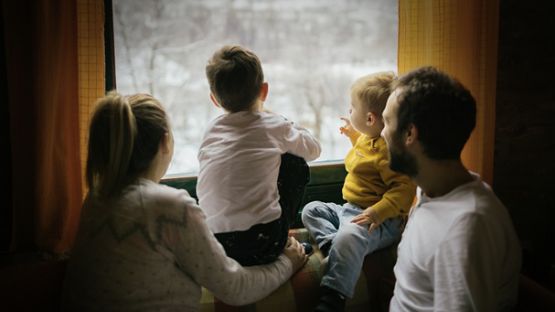 A young family sitting comfortable in a family room as snow falls outside of the window.