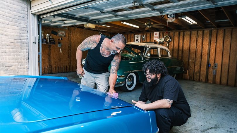 A father and son polishing and inspecting a blue vintage car in the garage.