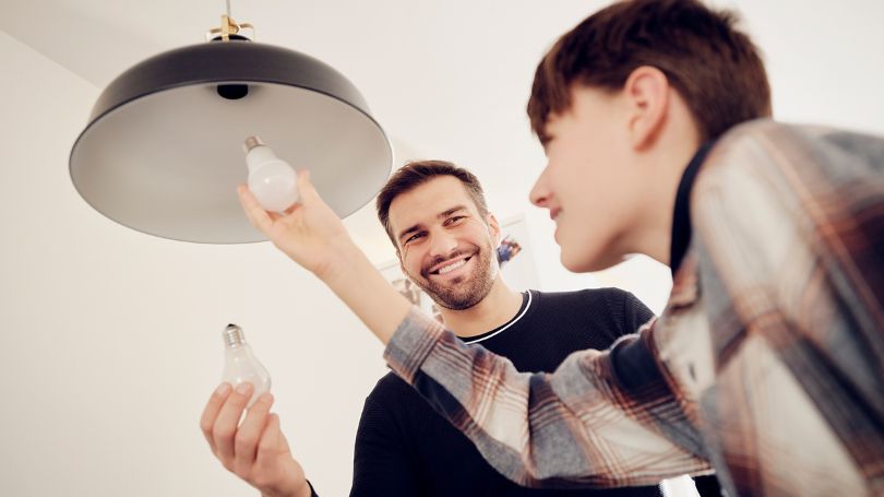 A father and son switching out a traditional light bulb with an LED energy-efficient light bulb. 