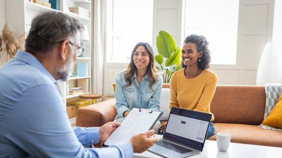 Un courtier explique patiemment les détails du contrat d'assurance à deux clientes.