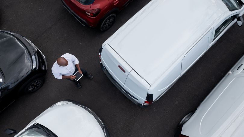 A person holding a tablet computer while looking at a van in a parking lot 