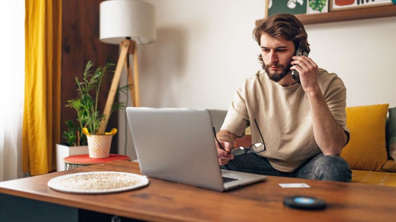 A photo of a late 20’s man sitting on a sofa with a laptop.