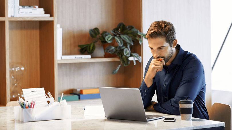 A man sitting at the kitchen breakfast bar looking at a laptop pensively looking up information about home insurance.