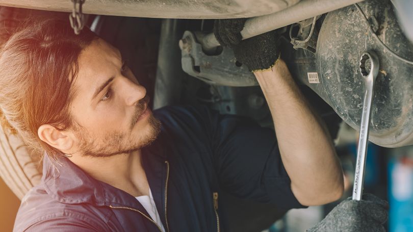 Male mechanic with wrench working underneath a vehicle