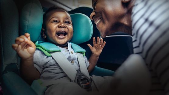 A mother putting a joyous one year old in a car seat.