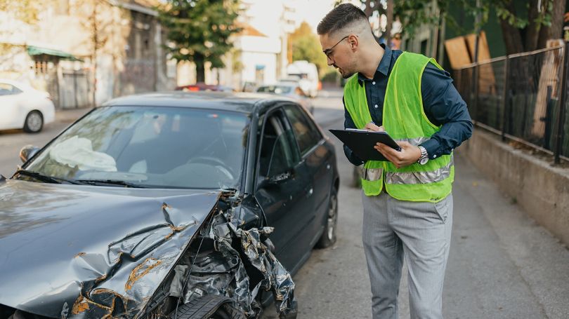 A person in a safety vest looking at a damaged car