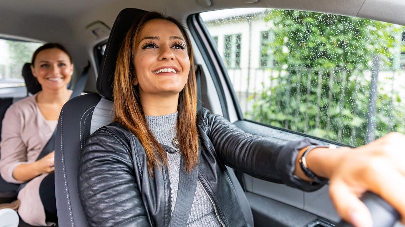 Ride-share driver in vehicle with smiling passenger in the back seat