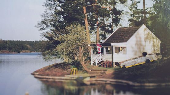 Chalet rustique au bord d’un lac arborant le drapeau canadien 