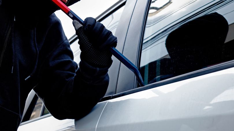 Masked thief trying to get into a car using a crowbar