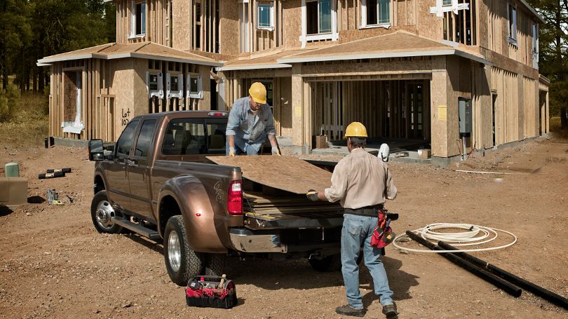 Two men lifting plywood onto a truck