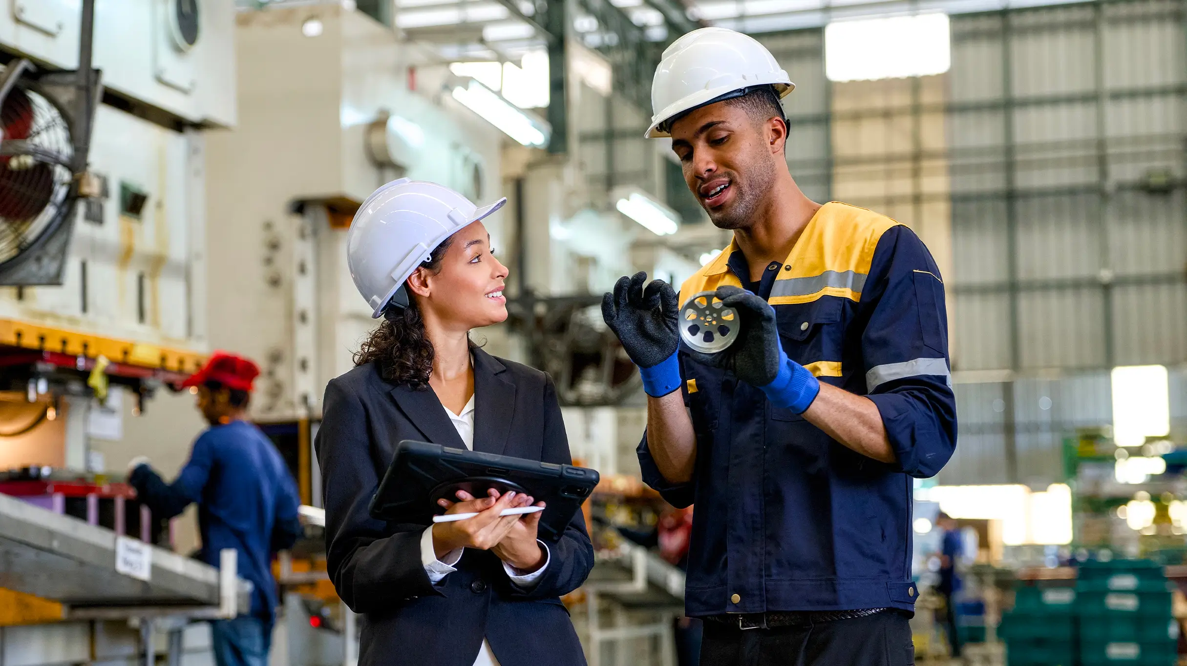 Woman and man discussing manufacturing component in factory, reviewing production quality, using a digital tablet