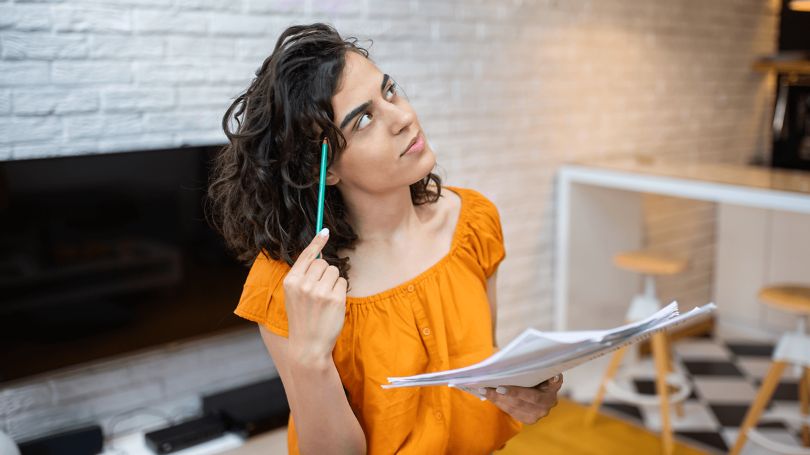 A woman looking around her house holding a pencil and paper wondering what’s not protected by most home insurance.