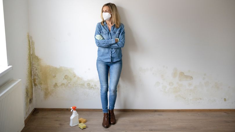 Young woman standing in front of white apartment wall with mold on it 