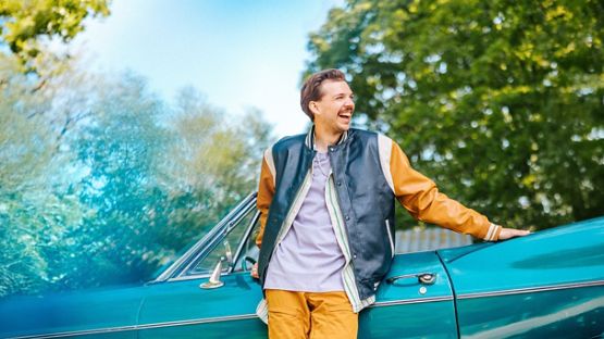 A young man leaning on a teal vintage car, waiting to hit the road.