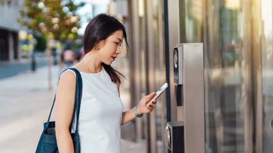 Security technology. Young woman scanning with smart phone before entering office building. 