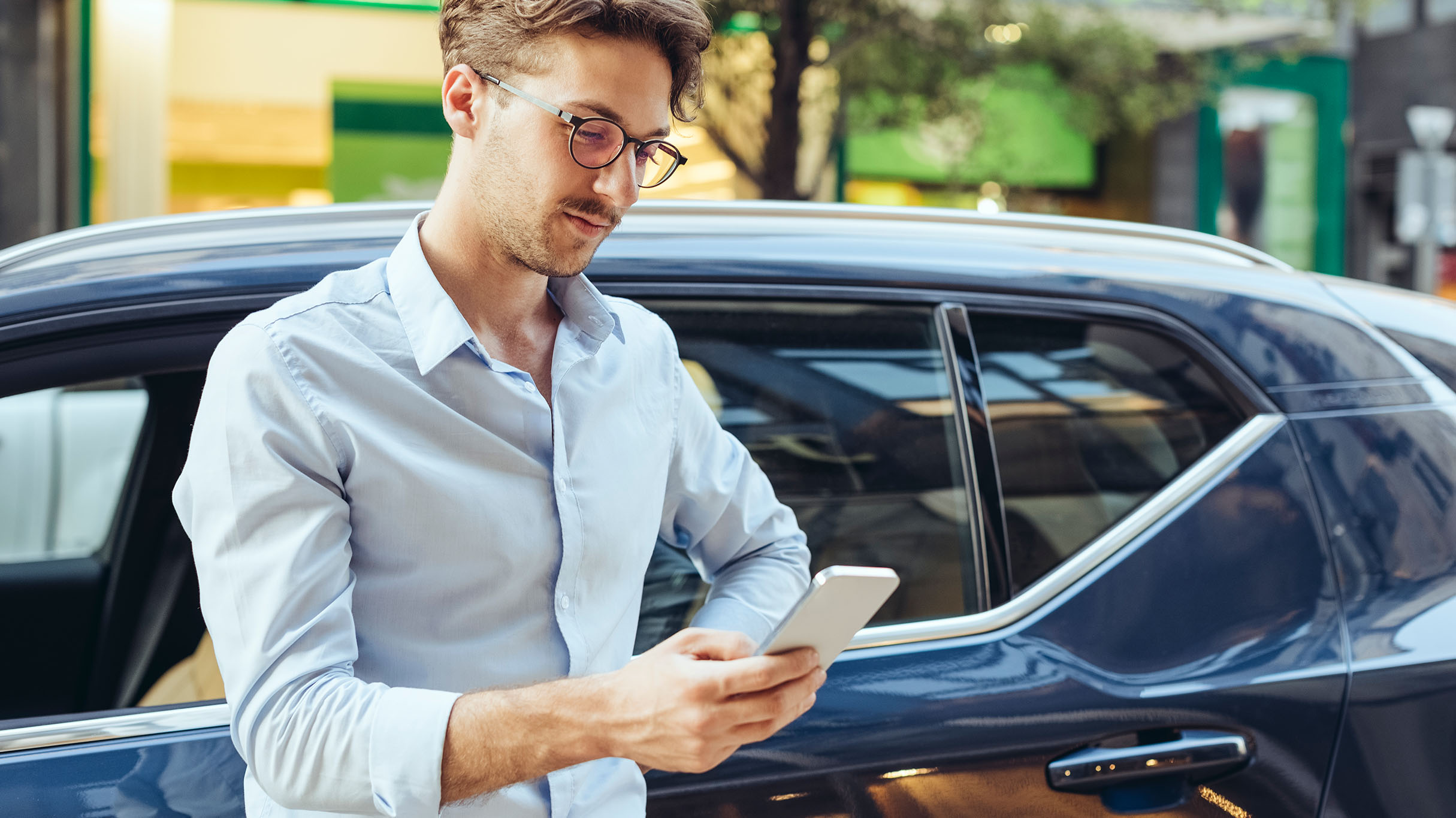 Driver checking his smartphone beside a car.