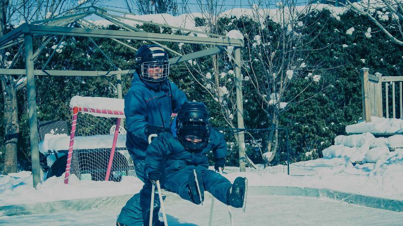 Two young kids skating on an ice rink with a hockey net behind them.