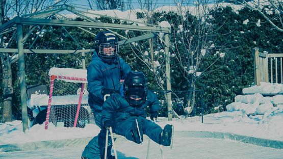 Deux jeunes enfants en train de patiner sur une patinoire, un filet de hockey derrière eux