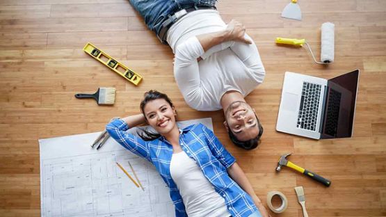 Un couple est couché sur le sol, avec à leurs côtés des outils destinés à la rénovation domiciliaire