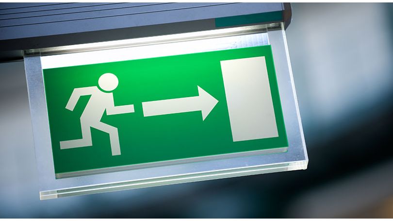 Close-up of a green emergency exit sign with an illustrated person running towards a door. 