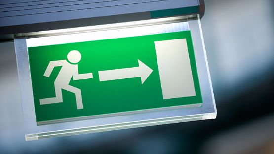 Close-up of a green emergency exit sign with an illustrated person running towards a door. 