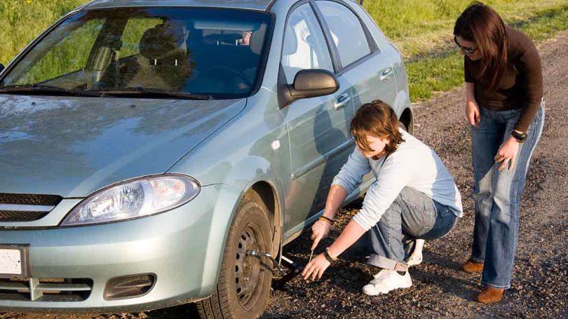 Amis en panne sur le bord de la route changeant un pneu à l'aide d'une trousse d'urgence.