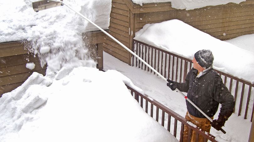 Un homme en train d’enlever la neige du toit d’une maison