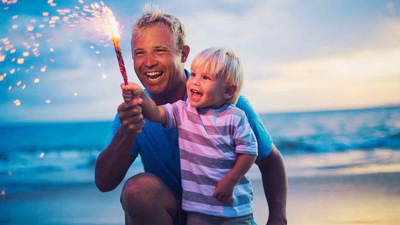 Père et fils s'amusant à utiliser des feux d'artifice et des cierges magiques en sécurité sur la plage.