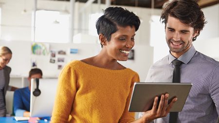 Deux collègues souriant et regardant un iPad.