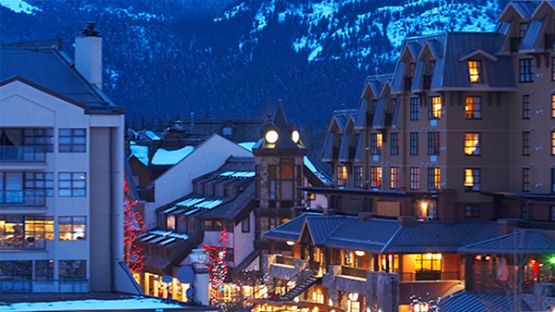 Snowy village with glowing lights at sunset.