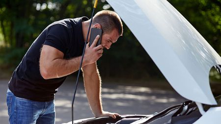 Conducteur examinant le capot de sa voiture en panne et appelant l'Indemnisation pour obtenir de l'aide. 