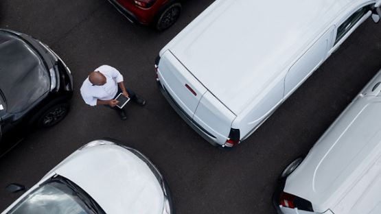 A person holding a tablet computer while looking at a van in a parking lot 