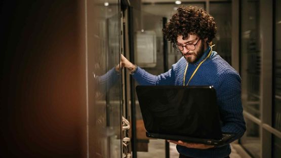 A person holding a computer and checking a computer network mainframe