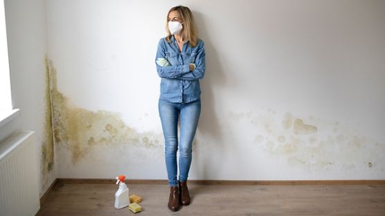 Young woman standing in front of white apartment wall with mold on it 