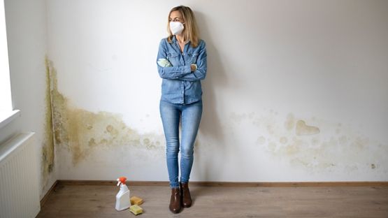 Young woman standing in front of white apartment wall with mold on it