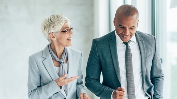 Two smiling business people walking through office hall and talking