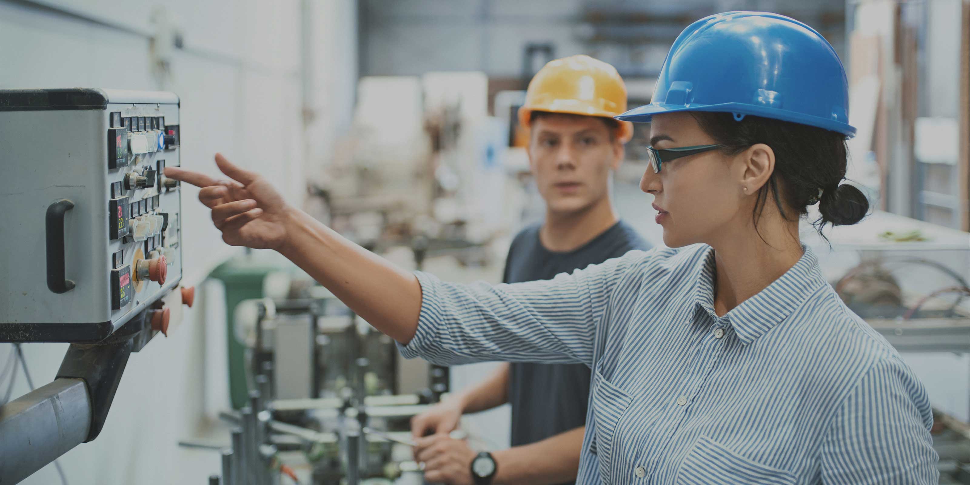 Workers wearing safety helmets inspecting equipment and a control panel in an industrial facility.