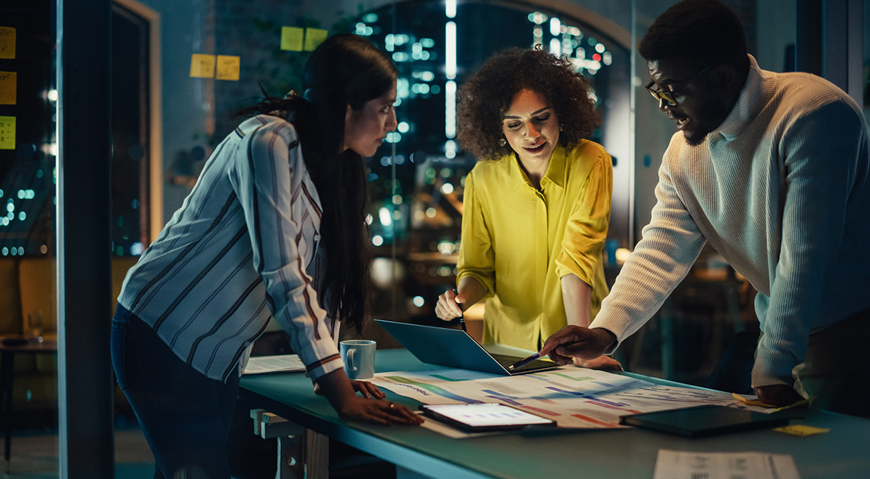 Three people in a business meeting having a discussion while looking at a laptop and printed documents