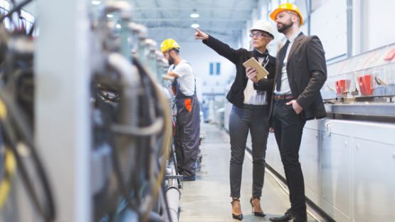 Male and female risk managers wearing hard hats assessing equipment in a facility.