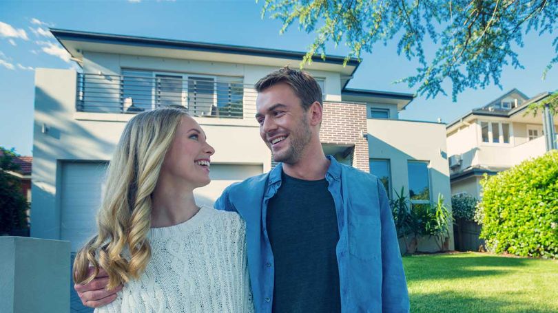 Couple souriant devant leur première maison.