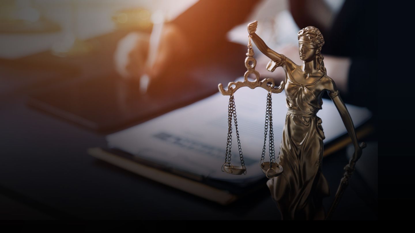 Statue of Justice holding a scale and lawyer working at a desk in the background