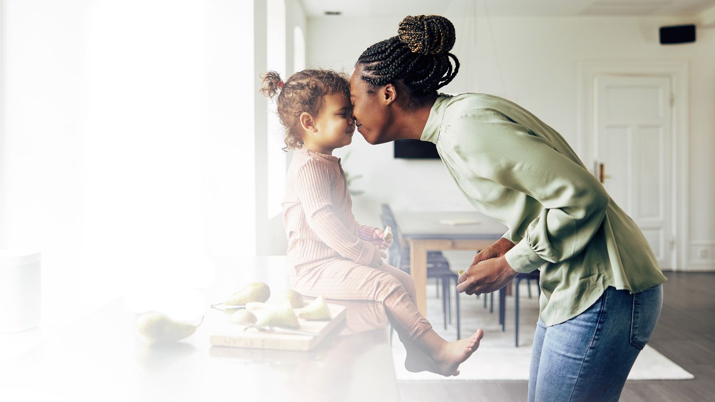 Une femme frottant son nez contre celui de sa fille dans leur cuisine à la maison.
