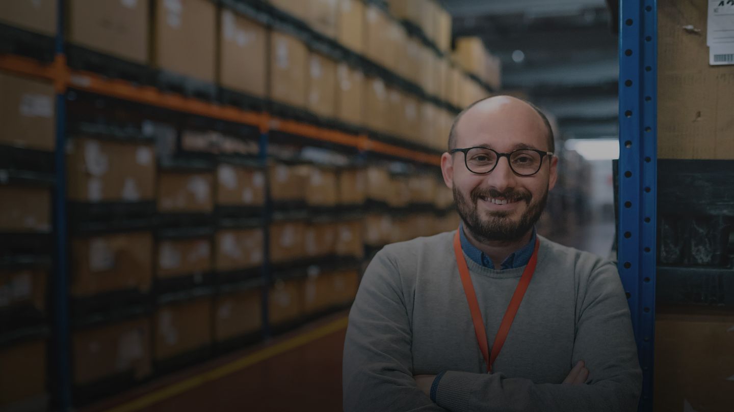 Man standing in warehouse with shelves full of boxes. 