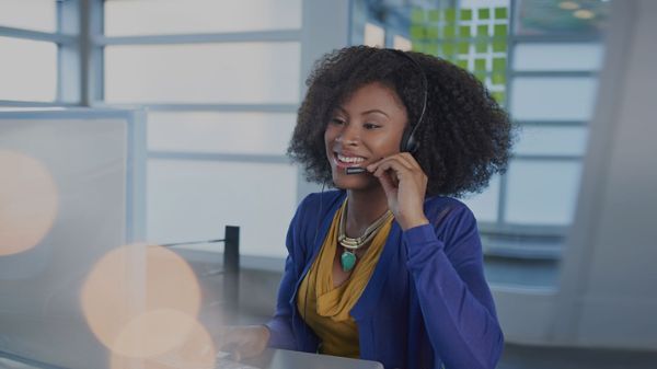 Smiling female customer representative wearing headphones working in an office.