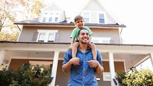 Père en train de promener son fils sur ses épaules à l’extérieur de leur maison nouvellement assurée.