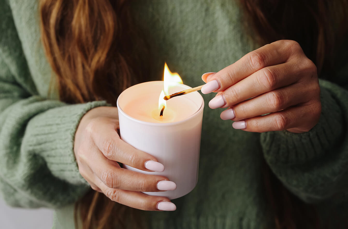Personne allumant une bougie avec une allumette tout en tenant la bougie dans ses mains à l’intérieur.